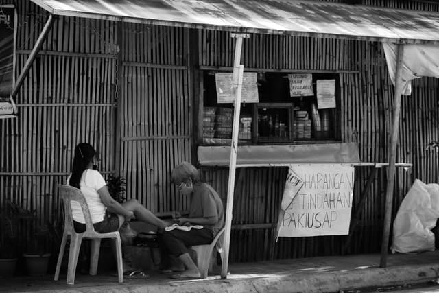 Black and white street photography capturing two adults engaging in commerce outside a bamboo store in Imus.