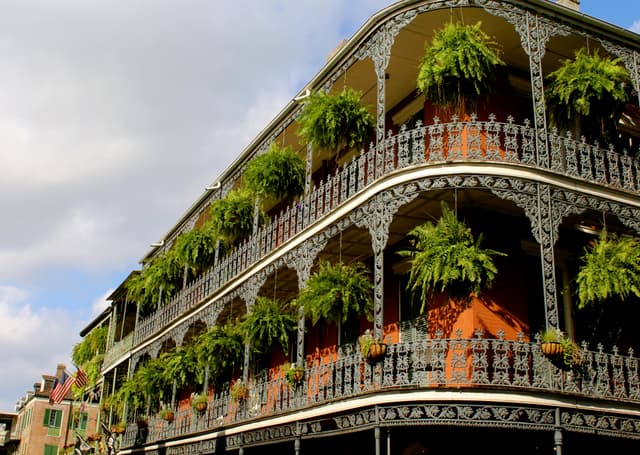 Detailed view of ornate ironwork balconies with lush greenery in New Orleans under a vibrant sky.