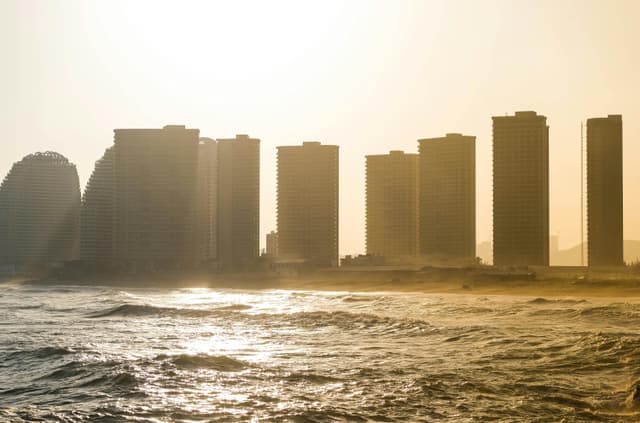 Sunset view of Huizhou's skyline with waves crashing on the coast, highlighting modern architecture.