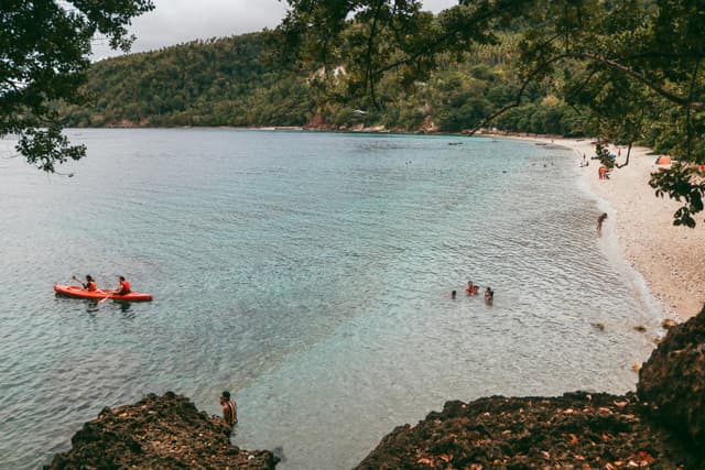 Relaxing day at the beach in Samal, Philippines, with people kayaking and swimming in clear waters.