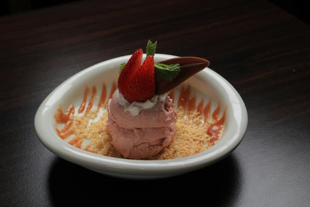Indulge in a strawberry ice cream dessert topped with fresh strawberries and chocolate shavings.