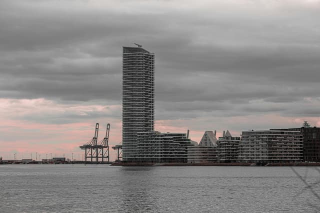 A dramatic cityscape of Aarhus, Denmark, showing modern architecture along the waterfront during a moody evening.