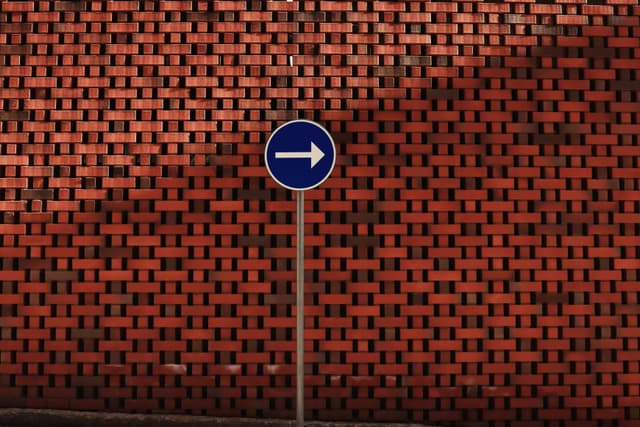 A blue right turn sign against a textured red brick wall in Norrköping, Sweden.