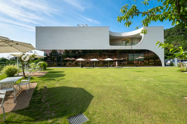 A modern cafe exterior with a spacious patio and lush green lawn, perfect for leisure and tourism.