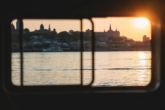 Scenic sunset view of Lévis, QC, from a boat window with cityscape and river reflections.