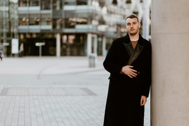 Man in a coat standing against a pillar in Manchester's urban setting.