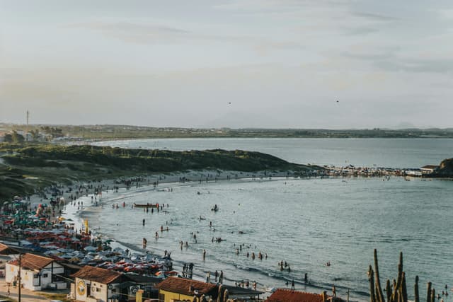 A scenic view of a crowded beach in Arraial do Cabo, Brazil, with people enjoying the seaside.