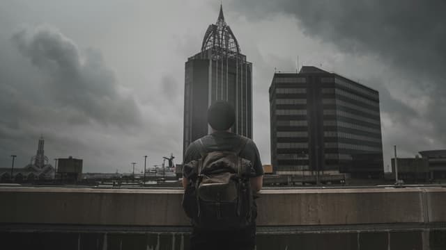 A man with a backpack overlooks the Mobile AL skyline under dramatic clouds.