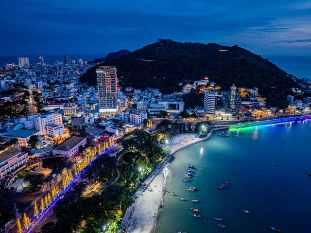 Stunning aerial view of a lively coastal city at night, illuminated by vibrant lights.