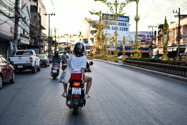 Motorcyclists ride through a bustling street in Chiang Rai, Thailand, showcasing urban life.