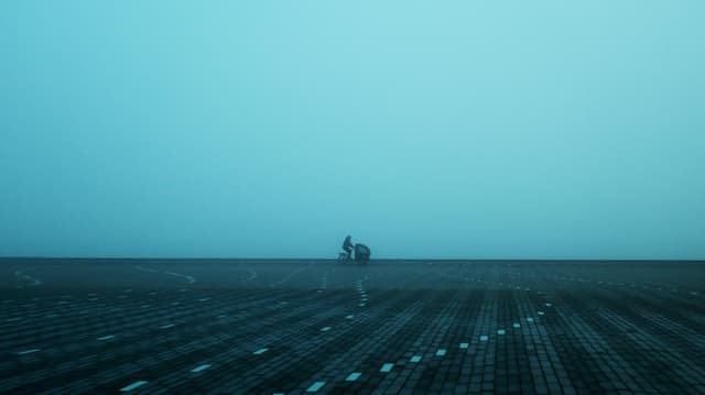 A misty scene in Aalborg, Denmark, featuring a lone cyclist on a paved square, evoking solitude.