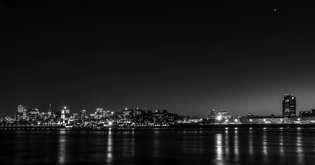 Stunning black and white panoramic view of Montreal's cityscape illuminated at night, reflecting on calm waters.