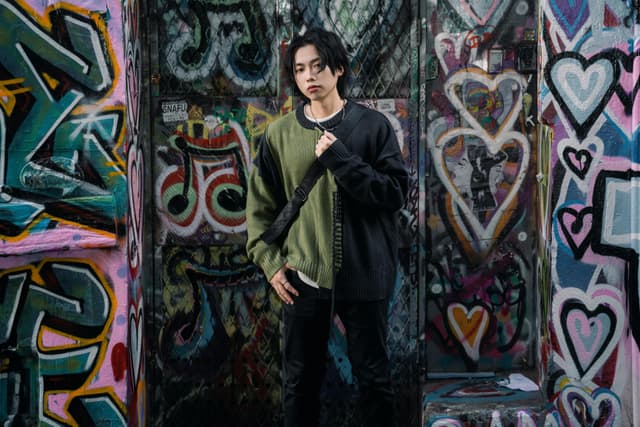 A stylish young adult poses against vibrant graffiti walls, showcasing street fashion.