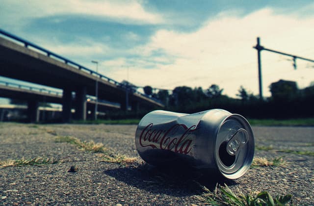 A close-up photo of an empty Coca-Cola can lying on an urban road, symbolizing litter.