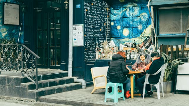 Three people enjoy a casual meeting at an outdoor cafe with a vibrant Starry Night mural backdrop.