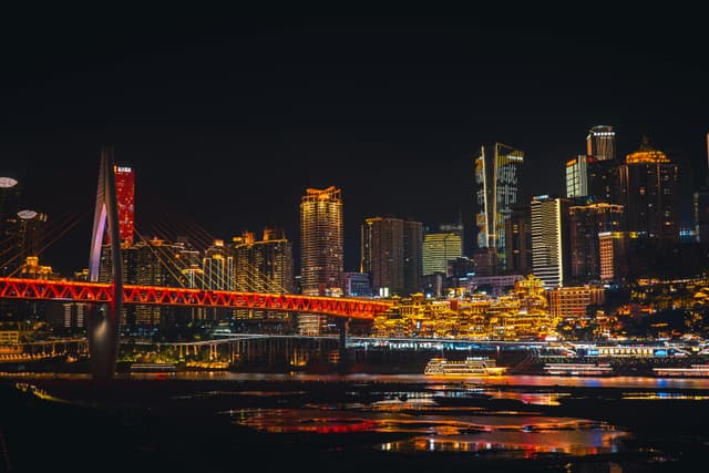 Stunning night view of Chongqing skyline with illuminated bridge over river, showcasing vibrant urban architecture.