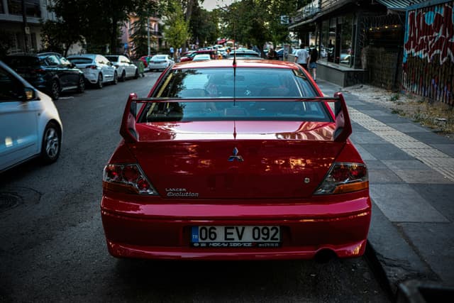 Red Mitsubishi Lancer Evolution parked on a city street with bustling urban background.