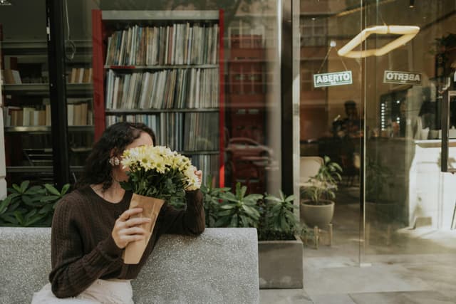 A woman holds a bouquet of flowers outside a contemporary urban café, capturing a serene moment.