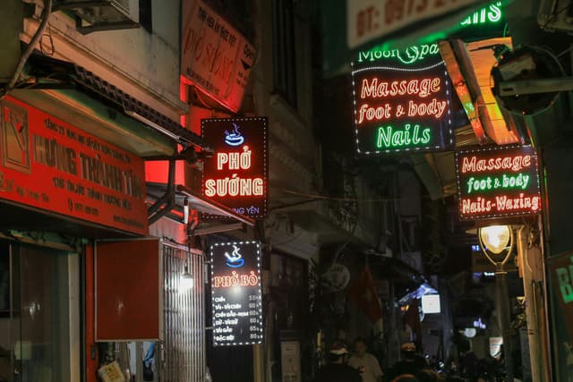 Colorful neon signs illuminate a bustling street in Hanoi, capturing the city's vibrant nightlife.