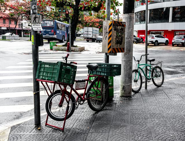 A rainy street corner in Santos, São Paulo with parked bicycles and traffic in the background.