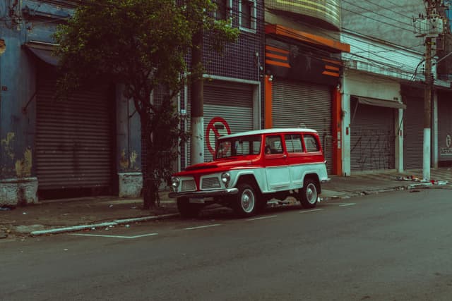 Classic red and white vintage jeep parked on an empty street with closed shops.
