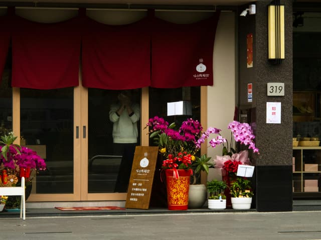 Colorful flowers adorn a shop entrance in Miaoli, Taiwan, creating a vibrant street scene.