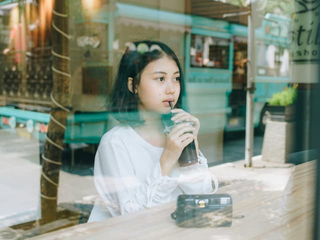 A young woman enjoys a drink at a cafe in Bandung, Indonesia, capturing a relaxed moment.