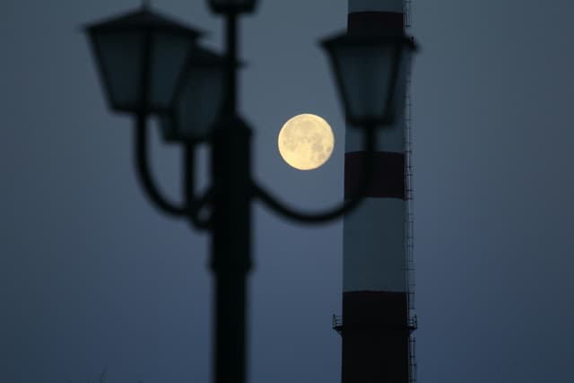 A vivid full moon set against the silhouette of a street lamp in an urban setting at night.