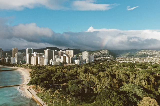 A stunning aerial view of Honolulu with skyscrapers, coastline, and lush greenery under a vibrant sky.