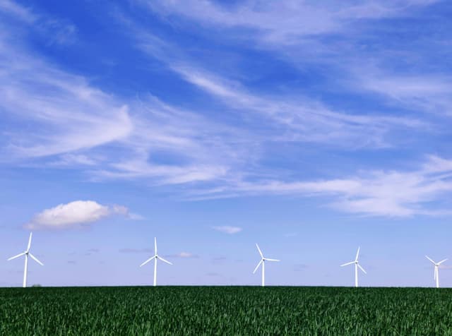 A row of wind turbines in a green field against a clear blue sky in Randers, Denmark.