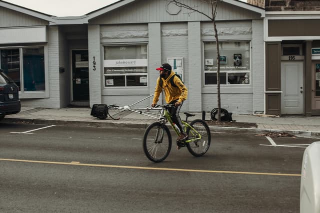 A cyclist in a yellow jacket rides a bike on a Milton street past a community building.