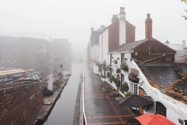A misty canal scene in Birmingham, UK, showcasing historic buildings along the waterside pathway.