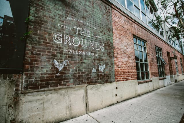 Rustic brick wall with The Grounds of Alexandria logo on a city street.