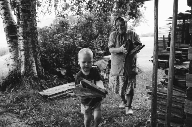 A touching black and white scene of a grandmother with her grandson gathering firewood outdoors.