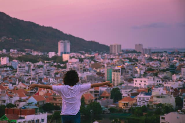 A woman stands with arms wide open overlooking the beautiful cityscape of Vũng Tàu at sunset.